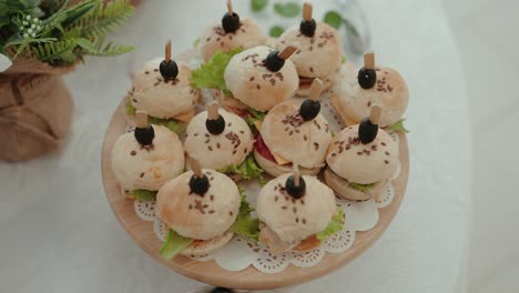 small gourmet burgers with lettuce and cheese topped with black olives on a round wooden tray