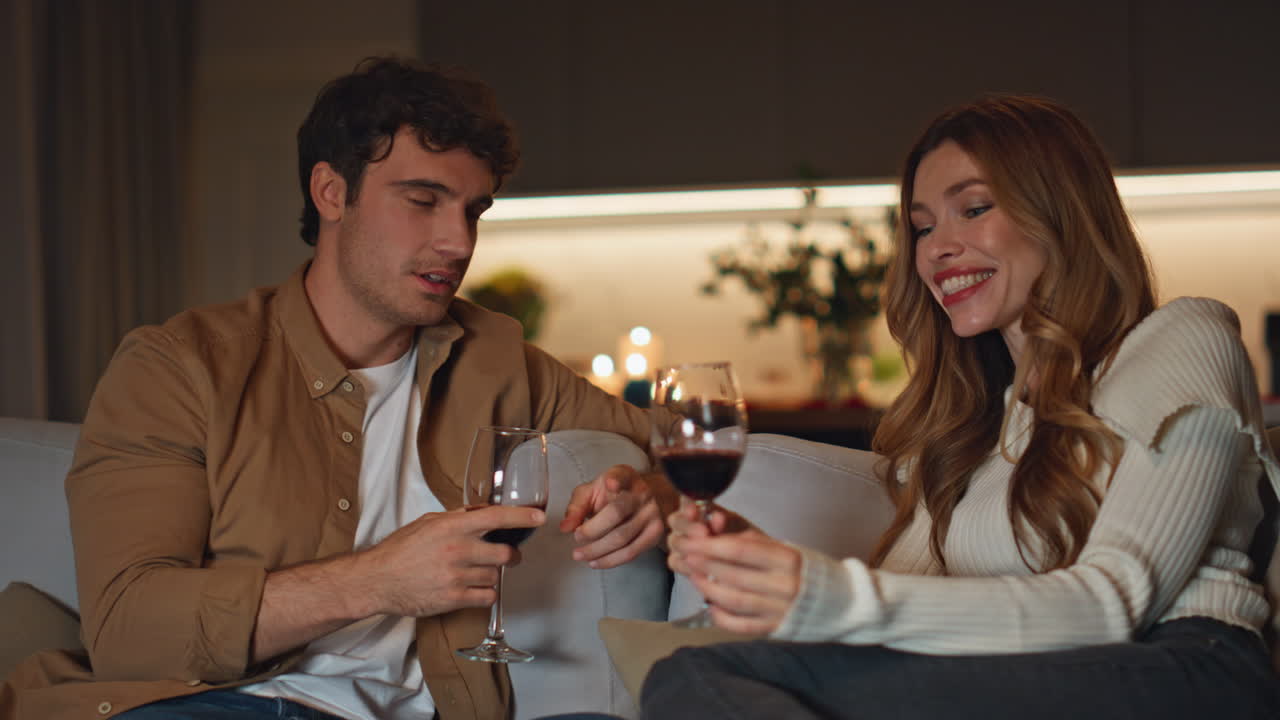 Coppia che si frequenta si gode l'intimità sul comodo divano di casa, con calici di vino in mano, in primo piano.