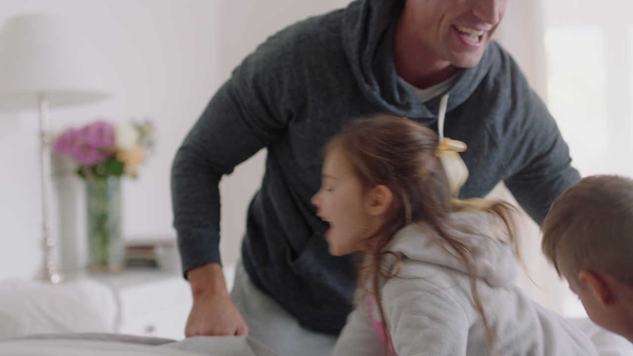 familia feliz con niños saltando en la cama jugando con la madre y el padre divirtiéndose en la mañana del fin de semana emocionados niños pequeños disfrutando del juego con los padres en casa imágenes de 4k