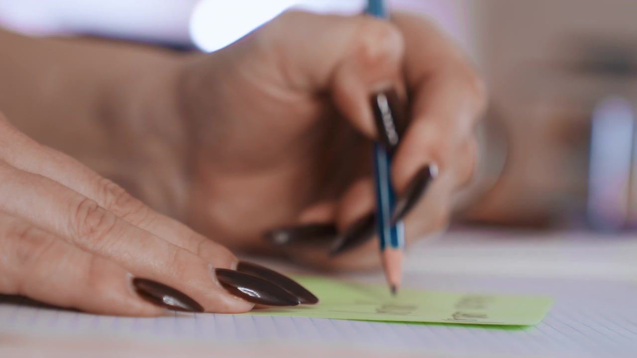 Closeup hand writing green sticky note dark manicure documenting home care visit details on lined notebook, gentle bokeh background, calm focused mood, caregiver preparing checklist for patient