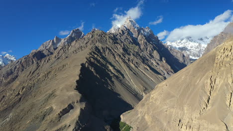 cinematic drone shot of tupopdan peak, passu cones in hunza pakistan, snow covered mountain peaks with steep cliffs, high wide aerial shot with shadows on the ridges