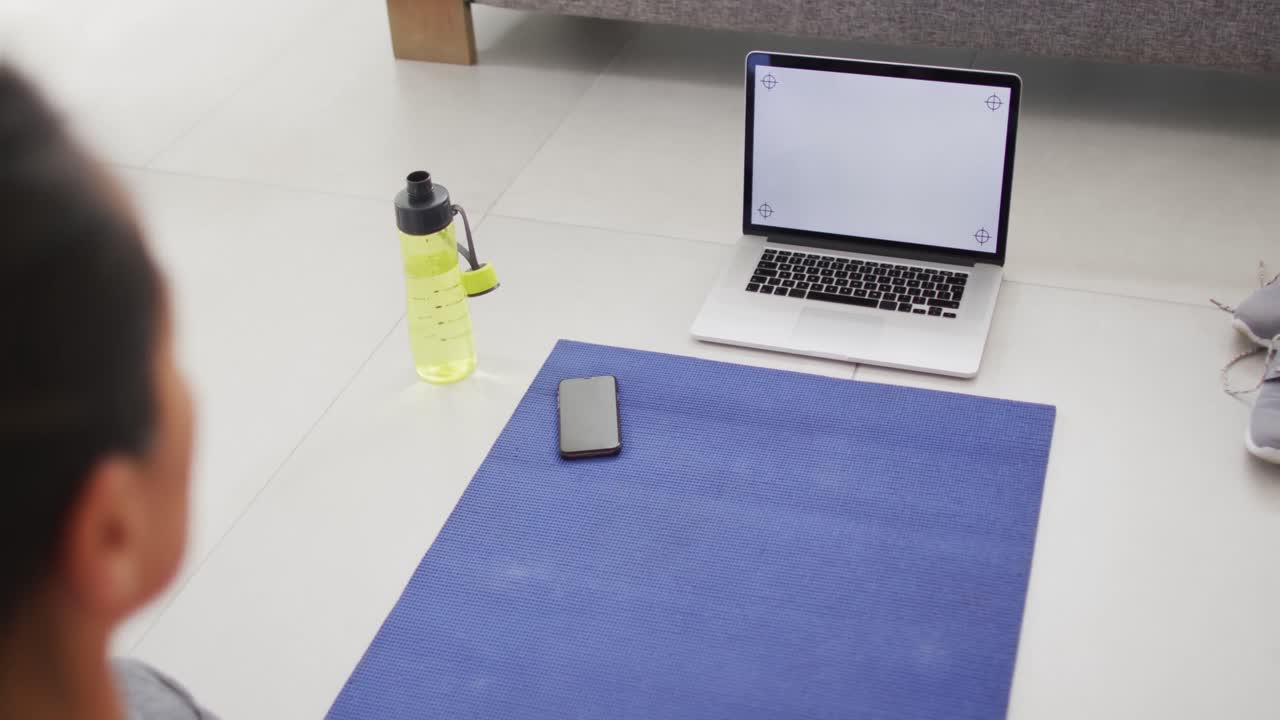 vista posterior de una mujer asiática en un tapete haciendo ejercicio con una computadora portátil con espacio de copia en la pantalla en casa