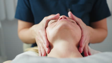 treatment provider cradles customer jawline gently in bright spa room with white background during relaxing facial massage therapy session highlighting expert hands and serene wellness environment