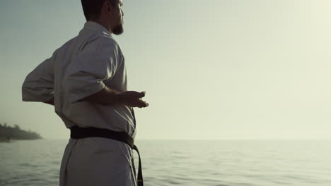 karate fighter enjoying sunset exercising on beach. man training near ocean.