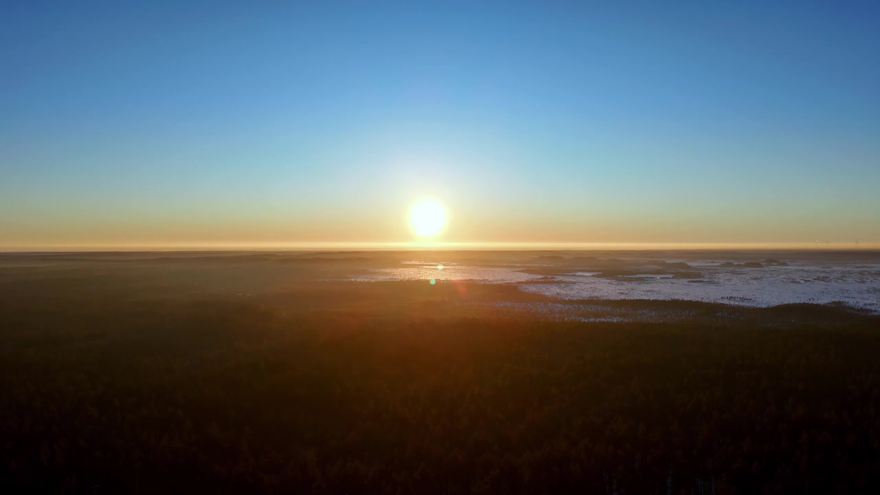 Aerial Wide View of Golden Sun Low Over Winter Horizon Illuminating Snow Covered Fields and Dark Evergreen Forests Under a Clear Blue Sky During a Peaceful Cold Morning Sunrise in Remote Northern Wild