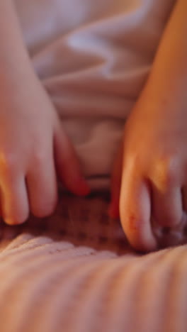Little kid unable to sleep picks pink knitted woolen plaid by small fingers on bed in semidark bedroom in evening extreme close view slow motion