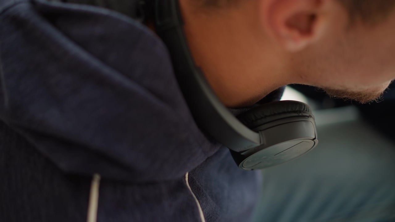 Close up of man wearing black headphones around his neck partially visible from side. subject is dressed in dark clothing with soft lighting highlighting fabric texture and ear details