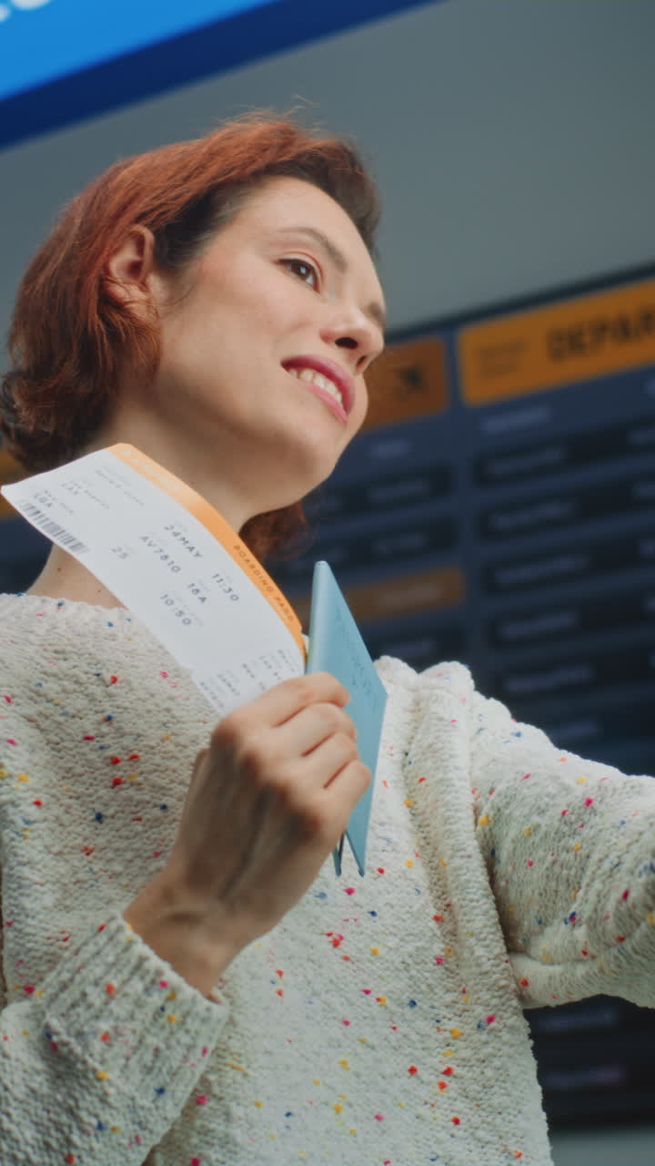 airport Terminal Happy Female Passenger Holding Plane Ticket Taking Selfie Using Smartphone Crowded Airport Terminal Shot of Happy Female Passenger Holding Plane Ticket Taking Selfie Using Smartphone Smiling at Camera Digital Flight Information Screen in the Background