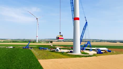 construction site with cranes, wind turbine in scenic field - drone shot