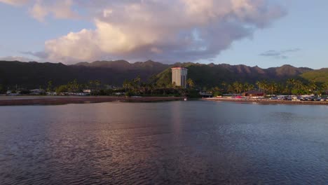 drone footage coming across the ocean at east honolulu showing one tall building on the edge of the mountain ridge in contrast to the single story infrastructure surrounding it pink alpenglow