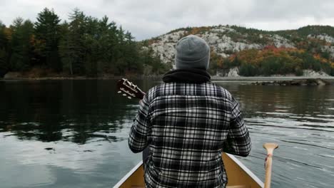 Man-plays-Ukelele-in-a-Canoe-in-Autumn-Leaf-Color-Forest-on-Canada-lake