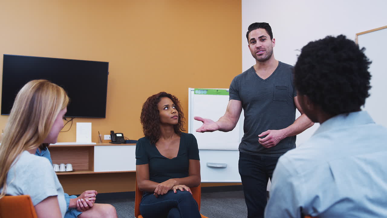 hombre de pie dirigiéndose a un grupo de hombres y mujeres en una reunión de terapia de grupo de salud mental