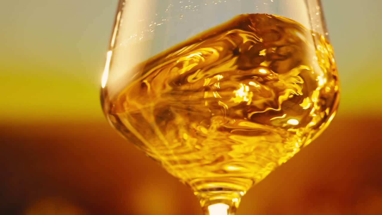 Orange or white wine bottle and glass against a sunset in a peaceful vineyard, pouring of ecological natural wine.