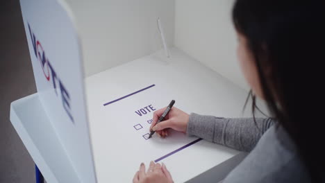 asian woman makes choice and votes in voting booth asian woman stands in voting booth at polling station makes choice and votes for presidential candidate or political party female voter fills out paper bulletin during elections civic duty concept