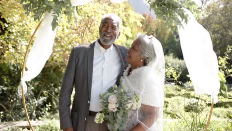 Portrait-of-happy-senior-biracial-couple-embracing-during-wedding-ceremony-in-garden,-slow-motion