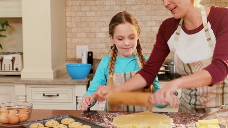 Smiling-mother-and-daughter-wearing-apron-rolling-dough-together-4K-4k