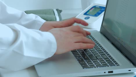 the concept of medicine, the doctor works, the hands of a man in a white coat print text on the laptop or write a pharmaceutical recipe, on a white table a tanometer
