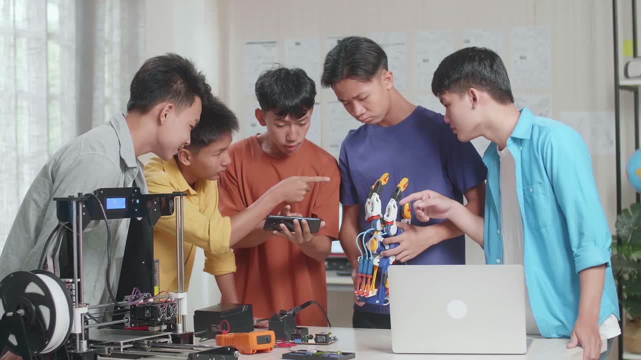 노트북과 3d 프린팅을 가진 젊은 아시아 소년 그룹이 집에서 일하는 동안 스마트 폰의 사진과 사이보그 손을 비교합니다.