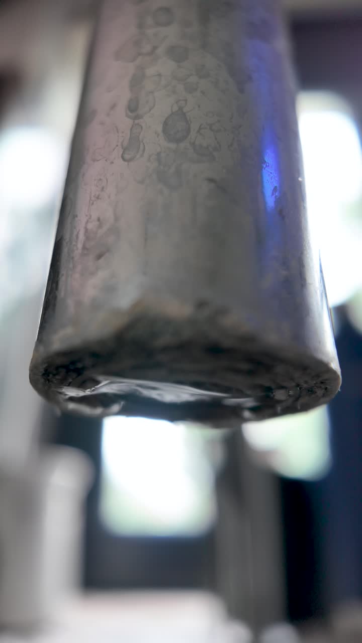 Close up of water dripping from a rusty tap, forming a large drop and highlighting water waste. slow motion, vertical video