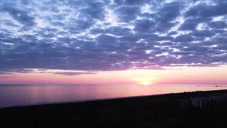 beautiful aerial vibrant high contrast pink purple sunset with blue clouds over baltic sea at liepaja, distant ships in the sea, wide angle descending drone shot camera tilt up slow zoom in