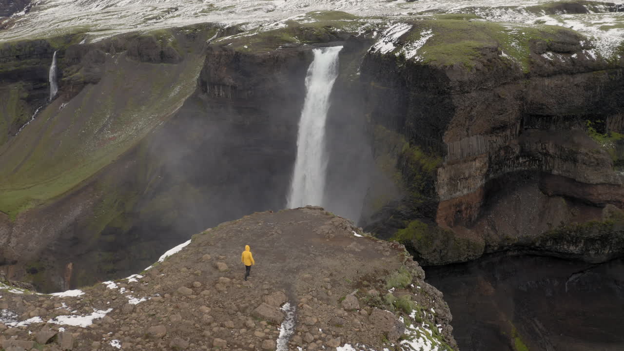 antena: un hombre con chaqueta amarilla caminando hacia la cascada de haifoss en islandia