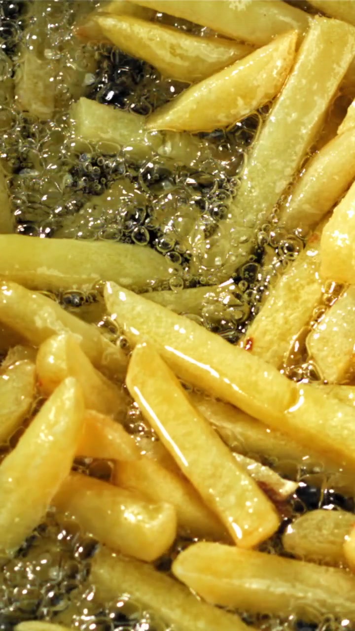 Patatas fritas doradas friéndose en aceite caliente burbujeante.