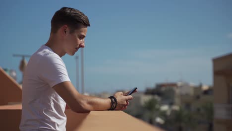 hombre relajado usando un teléfono inteligente en un balcón en un hermoso día