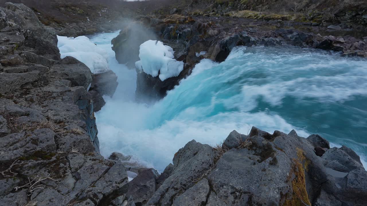 fuerte y poderoso flujo de agua azul en la superficie rocosa de la cascada hlauptungufoss en el río bruara, islandia - disparo de drones