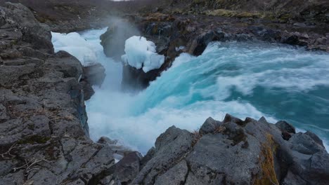 strong and powerful flow of blue water in rocky surface of hlauptungufoss waterfall in river bruara, iceland - drone shot