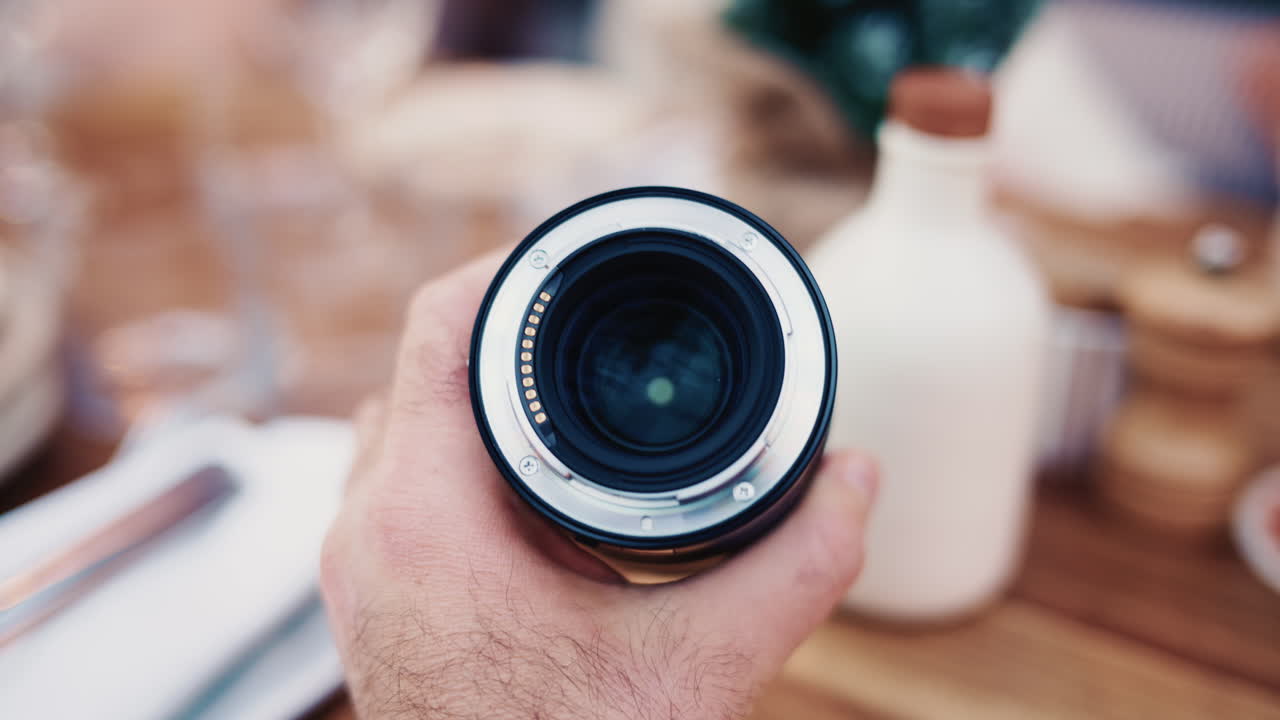 Primo piano dell'obiettivo di una fotocamera tenuto in mano con un effetto bokeh sullo sfondo.