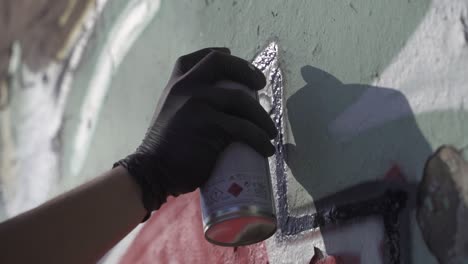 close up shot of a hand wearing black gloves painting graffiti on wall