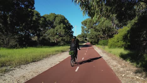 A-woman-riding-a-bike-in-a-red-bike-line-inside-a-public-greenery-park-in-a-blue-sky-sunny-day-in-Coogee,-Perth---Western-Australia