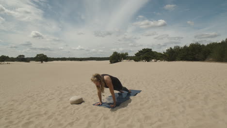 Mujer-Moviéndose-Hacia-La-Pose-De-Un-Niño-De-Yoga-En-Las-Dunas-De-Arena