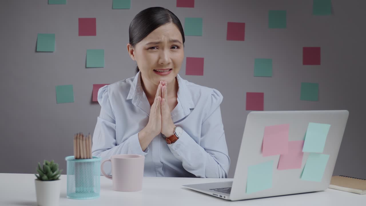 가정 사무실에서 일하는 아시아 여성이 손을 잡고 기도하고 카메라를 쳐다보고 있습니다.