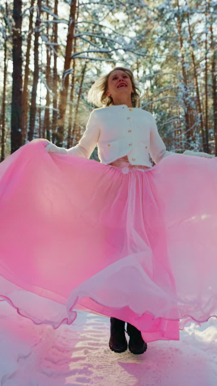 Donna gioiosa in gonna rosa che volteggia in una foresta invernale innevata.