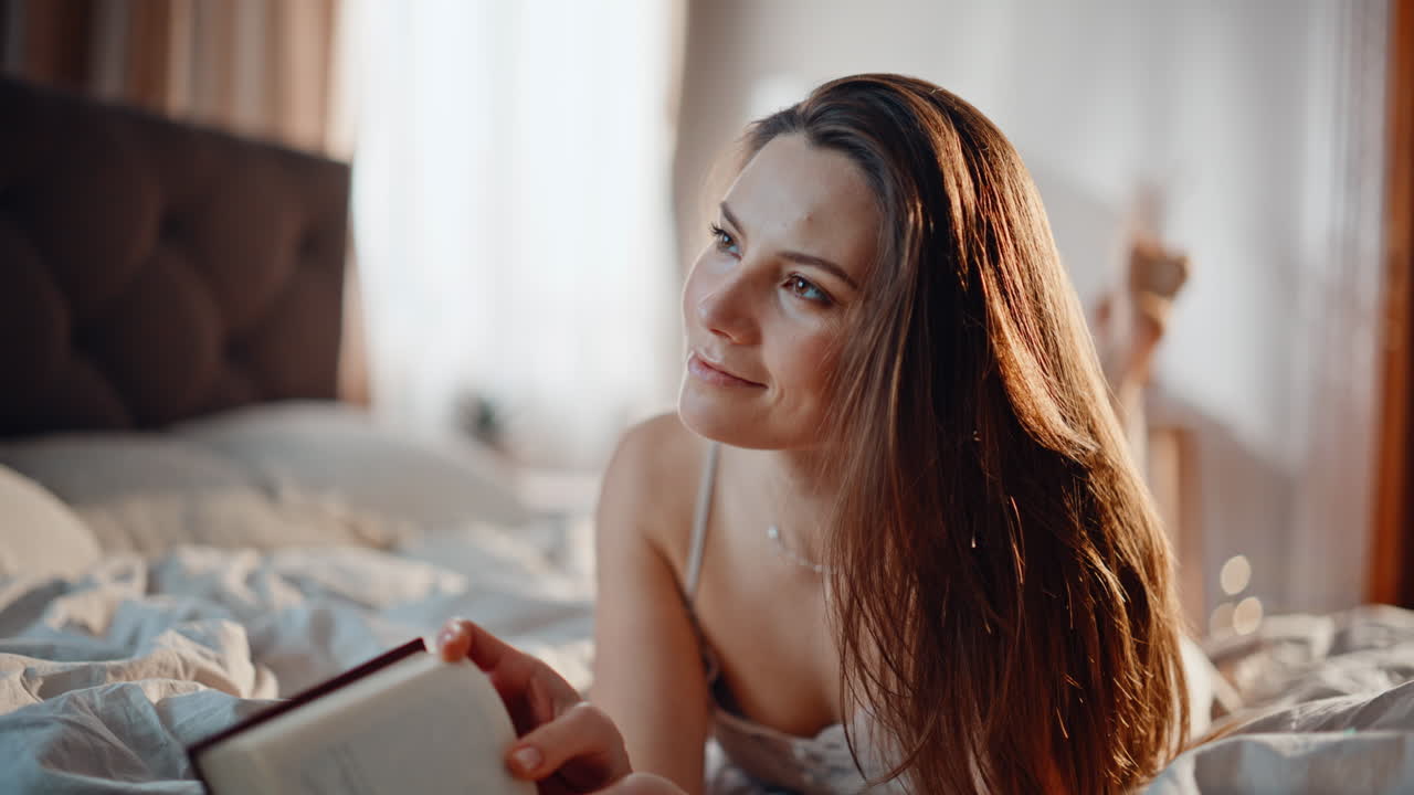 Mulher lendo um livro na cama, aproveitando uma manhã tranquila e aconchegante em casa em close-up. Morena relaxada