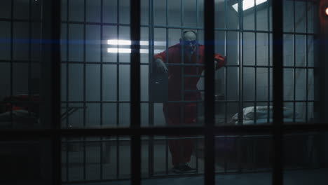 Close-Up-of-Prisoner-in-Orange-Uniform-Holding-Metal-Bars-in-Prison-Cell----------(Stock-Footage)