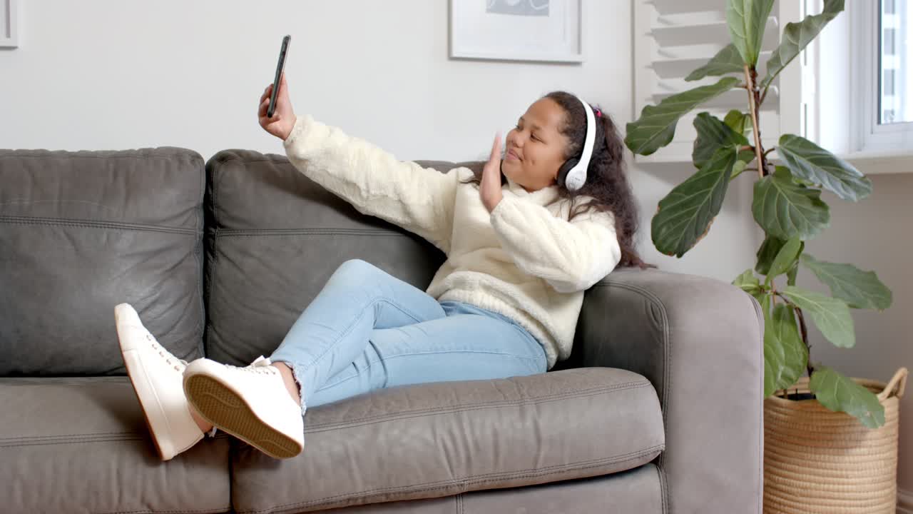 Bambino sdraiato sul divano a casa che scorre lo smartphone, toccando le cuffie per la musica, e posando per un selfie.