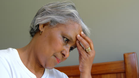 Side-view-of-old-black-senior-woman-sitting-on-bed-with-hand-on-forehead-in-comfortable-home-4k