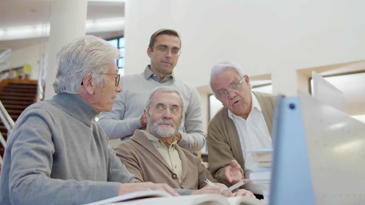 hombres mayores y profesores mirando la pantalla de la computadora portátil en la biblioteca