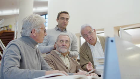 senior men and teacher looking laptop screen in library