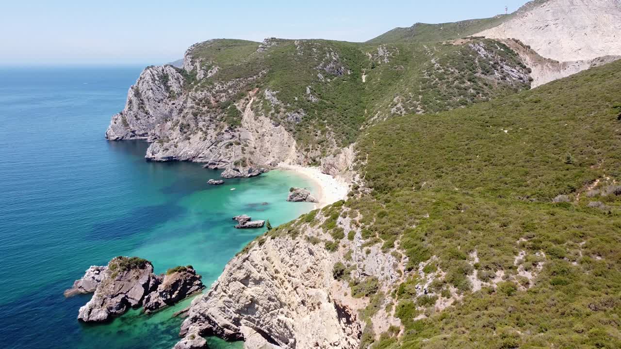 vista aérea de drones de la playa de ribeira do cavalo en sesimbra, portugal - volando sobre la costa con montañas rocosas verdes, océano atlántico azul y playa de arena escondida