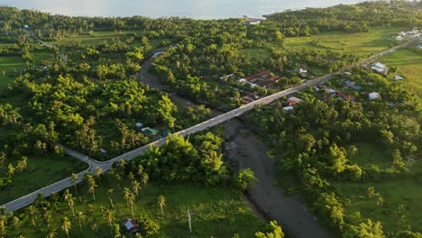 aerial flyover shot of island province road and bridge over shallow river amid lush tropical greenery - san andres, catanduanes, philippines