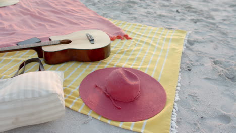 a guitar and a pink hat rest on a beach blanket, with copy space