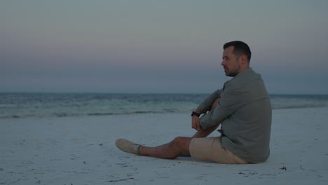 lonely man sits in silence on pure white sand tropical beach contemplating the beauty of the ocean during twilight