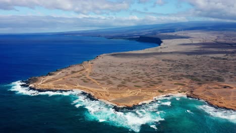 the coastline unfurls where hardened lava meets the pacific ocean, revealing a stark and rugged transition from sea to arid inland plateau under a wide tropical sky