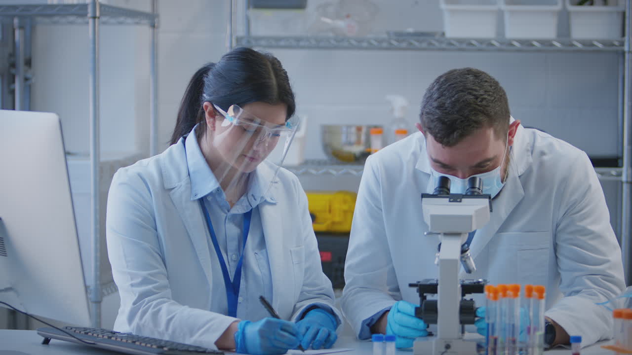 trabajadores de laboratorio masculinos y femeninos que llevan a cabo investigaciones utilizando el microscopio y registran los resultados en computadora