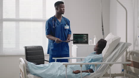 In-the-Hospital-african-american-beautiful-doctor-checking-on-woman-patient-lying-down-on-hospital-bed-talking-to-her-both-smiling