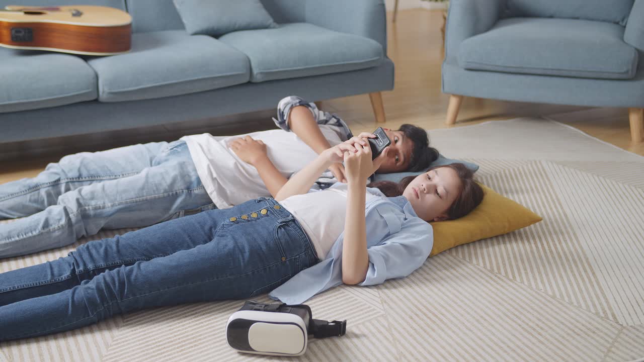 집에서 바닥에 카에 누워있는 십대 아시아 커플: 화가 난 소녀가 스마트폰을 사용하고 남자친구를 무시하고, 화가 난 남자친구가 그녀에게 관심을 기울이려고 시도 한 후 그릴 친구를 혼자 떠난다.