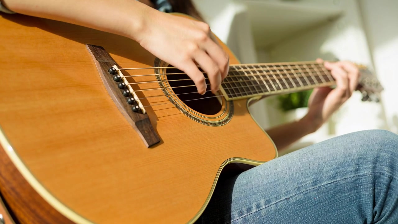 Gitarzystka opierająca dłoń, szarpiąca struny gitary akustycznej na kolanach w domu, w dżinsach, ćwicząca.